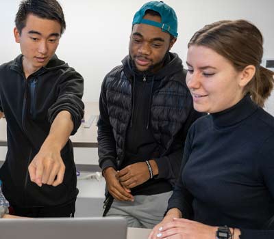 3 students gathered around a laptop