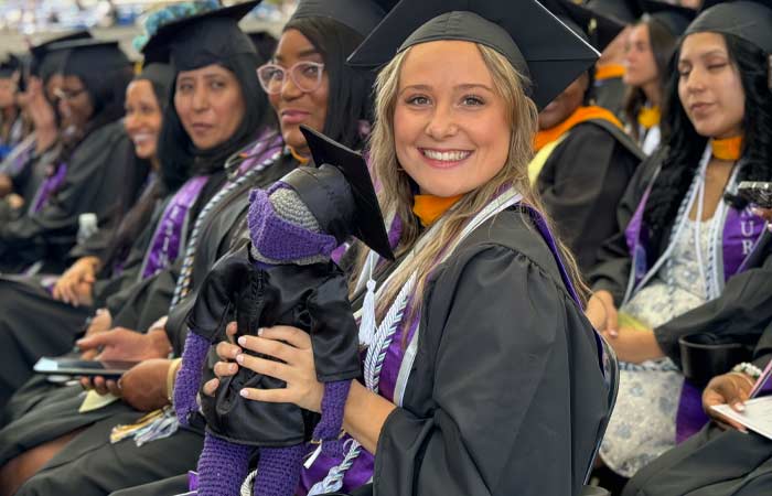 smiling grad at Commencement holding a crocheted mascot