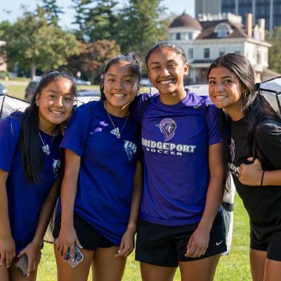 group of 4 smiling students carrying duffle bags