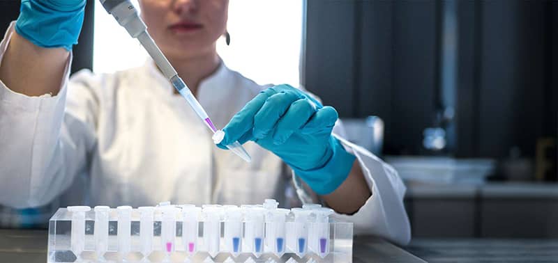 scientist pipetting colored chemicals into a tube